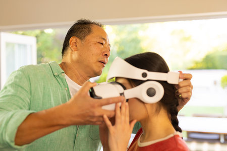 Adjusting VR headset, father helping girl experience virtual reality at home. technology, gaming,...