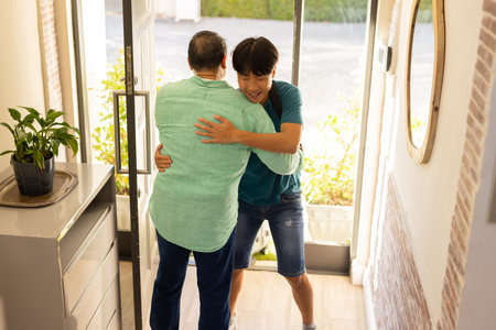 Hugging each other, asian father and son greeting warmly in home entrance hallway. friendship, togetherness, warmth, affection, relationship, interactionの写真素材