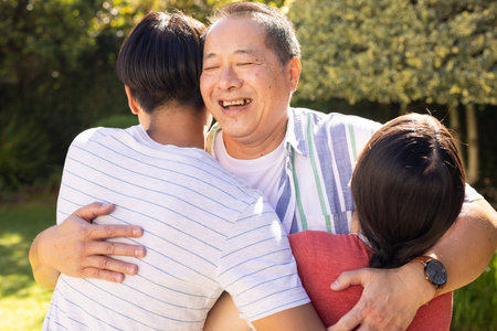 Smiling father hugging teenage son and daughter outdoors, enjoying quality time together. happiness, bonding, togetherness, affection, leisureの写真素材