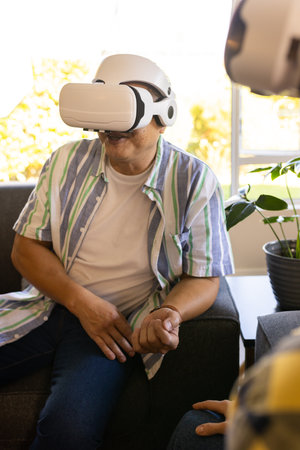 Using VR headset, man sitting on couch in living room, enjoying virtual experience. Virtual reality, technology, immersive, entertainment, relaxation, digitalの写真素材