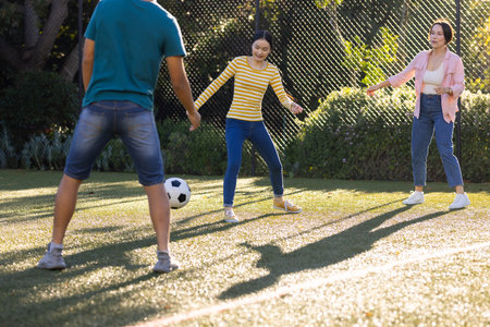 Playing soccer outdoors, asian family enjoying time together on sunny day. sports, fun, activity,...