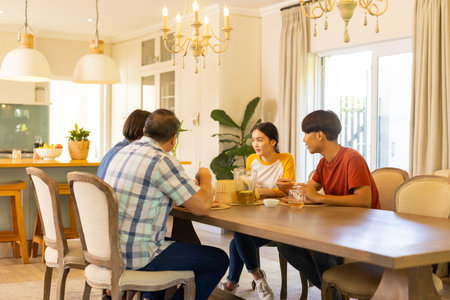 At home, asian family enjoying meal together, sitting at dining table and talking happily. togetherness, happiness, bonding, conversation, home, gatheringの写真素材