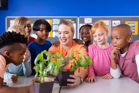 In school, female teacher showing potted plants to diverse group of curious diverse students. Education, learning, botany, classroom, teaching, diversityの写真素材