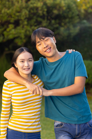 Smiling young asian brother and sister hugging and posing together outdoors in garden. family, bonding, happiness, togetherness, joyful, natureの写真素材