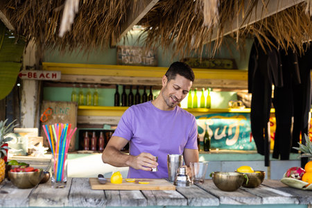 Happy biracial barman preparing cocktail at beach. Spending quality time, lifestyle, summertime and...
