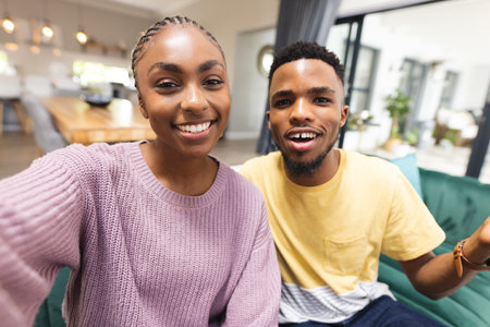 Happy african american couple sitting on sofa and having video call in living room. Spending quality...