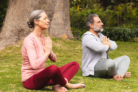 Meditating outdoors, mature couple sitting cross-legged in peaceful moment. Meditation, tranquility, wellbeing, mindfulness, serenity, relaxationの写真素材