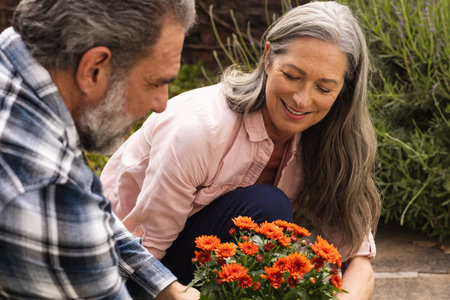 Planting vibrant orange flowers, mature couple gardening together, smiling outdoors. nature, horticulture, landscape, teamwork, hobbies, leisureの写真素材