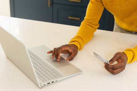African american man shopping online using laptop and credit card at home. E-commerce, online...