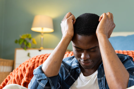 At home, African American man feeling stressed, sitting on couch with hands on head. anxiety, mental...