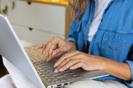 Woman in denim shirt typing on laptop at home, focusing on work. Remote working, home office, technology, concentration, productivity, casualの写真素材