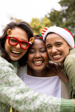 Christmas time, wearing festive hats, multiracial friends outdoors embracing. friendship, celebration, togetherness, party, happiness, bondingの写真素材