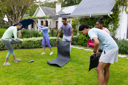 Young multiracial friends setting up yoga mats for outdoor exercise in garden. Fitness, wellness,...