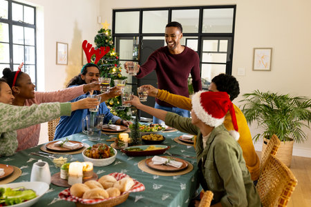 multiracial friends celebrating Christmas together, toasting around festive dinner table at home. Celebration, holiday, gathering, friendship, tradition, diningの写真素材