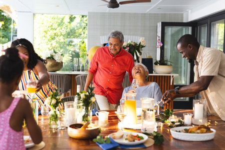 Multiracial family enjoying joyful meal together , sharing laughter and drinks, in garden. dinner, bonding, celebration, happiness, togetherness, gathering
