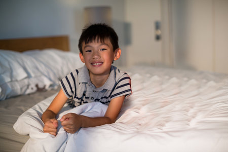 Smiling boy relaxing on bed at home, enjoying cozy morning light, copy space. Childhood, relaxation,...