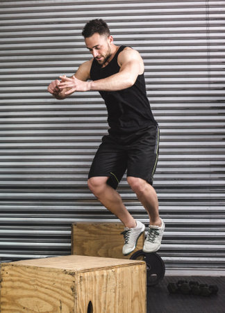 Man performing box jump exercise in gym, focusing on strength and agility. Fitness, workout,...
