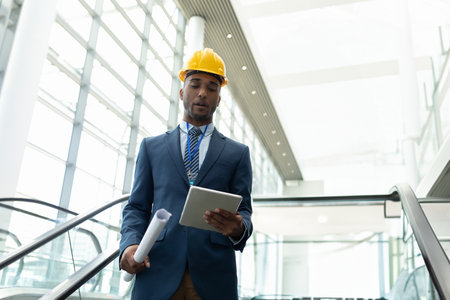 Engineer in suit and hard hat reviewing plans on tablet in modern building, copy space. Architecture, construction, technology, professional, planning, businessの写真素材