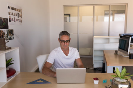 Man in office working on laptop, wearing glasses, focused on task, copy space. Business,...