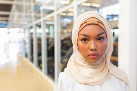 Confident woman in hijab standing in modern office, looking at camera, copy space. Business,...