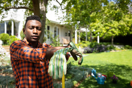 Man in garden putting on gloves, preparing for outdoor gardening work. Gardener, horticulture,...