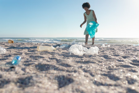 Collecting plastic waste on sandy beach, African American woman promoting environmental care, copy...