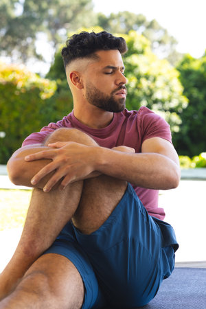 Man relaxing outdoors, sitting on yoga mat, enjoying peaceful moment in garden. Relaxation,...