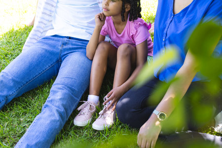 Family relaxing on grass, young girl sitting between parents, enjoying sunny day. relaxation,...