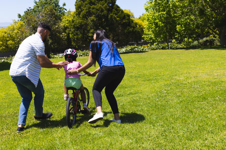 Parents teaching child to ride bicycle in sunny park, enjoying family time. Parenting, cycling, outdoor, bonding, leisure, recreationの写真素材