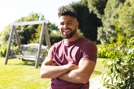 Smiling man enjoying sunny day in garden with wooden swing in background. Outdoor, relaxation, leisure, nature, happiness, maleの写真素材