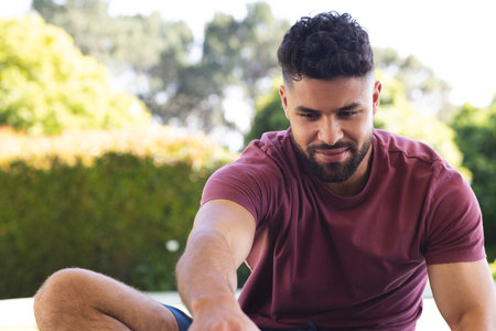 Smiling man enjoying outdoor picnic, reaching for food on sunny day. outdoors, summer, relaxation, leisure, nature, happinessの写真素材