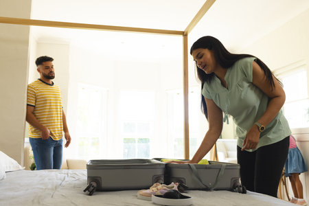 Woman packing suitcase on bed while man watching in bright bedroom. Travel, vacation, preparation, couple, journey, luggageの写真素材
