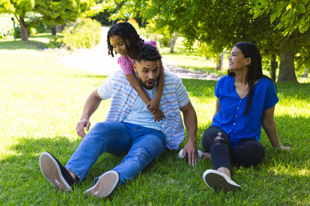 Family enjoying playful moment in park, daughter riding on father's back. bonding, fatherhood, happiness, childhood, outdoor, recreationの写真素材