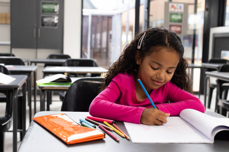 In school, young girl drawing with colored pencils at classroom desk, concentrating, copy space....