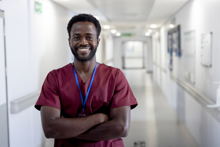 Confident male nurse in scrubs smiling in hospital corridor, arms crossed. Healthcare, professional, medical, caregiving, uniform, confidenceの写真素材