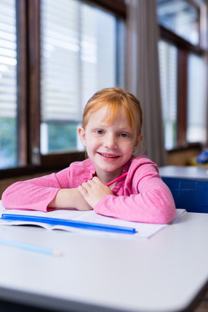 Smiling girl sitting at desk with open book in school classroom. Education, learning, studying,...