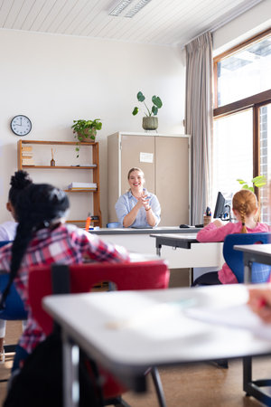 Female teacher clapping hands, engaging diverse students in classroom during school lesson....
