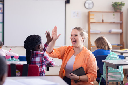 High-fiving african american girl in classroom, female teacher celebrating achievement in school. Education, celebration, success, encouragement, teamwork, motivationの写真素材