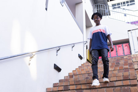 Walking down stairs, african american boy in casual clothes at school, looking confident.