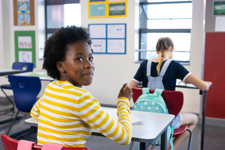 In school, african american girl in striped shirt sitting at desk, looking back and smiling....