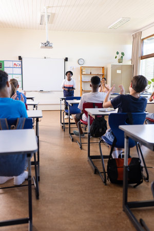 Female teacher leading classroom discussion with students sitting at desks in school. Education, teaching, learning, interactionの写真素材
