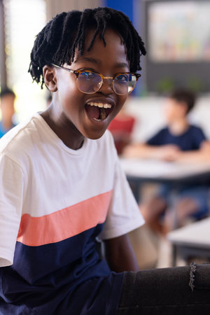 In school, excited student wearing glasses smiling in classroom with classmates. Education, friends,...