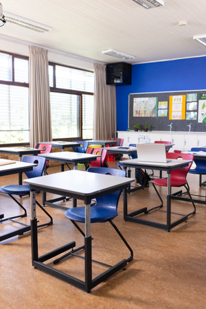 Empty classroom with colorful chairs and desks arranged neatly for students, copy space. Education,...