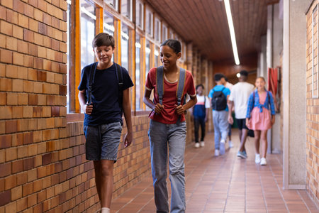 Walking in school hallway, students with backpacks talking and smiling. Education, conversation, friendship, youth, learning, campusの写真素材