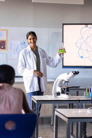 In school, Indian female teacher holding flask and explaining science experiment to students....