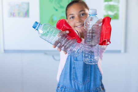 Holding plastic bottles, girl smiling in school classroom. Recycling, environment, education,...