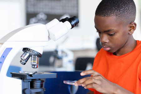 Using microscope, student examining petri dish in school science classroom. Laboratory, research,...