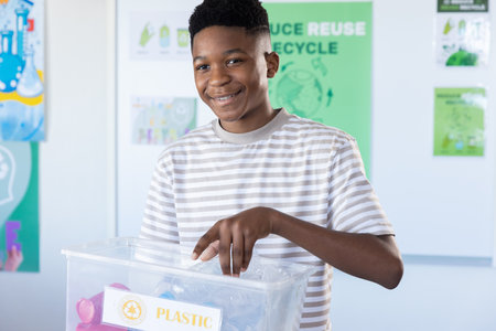 Recycling plastic, boy smiling and holding bin in school classroom. Sustainability, environment, eco-friendly, education, conservation, waste managementの写真素材