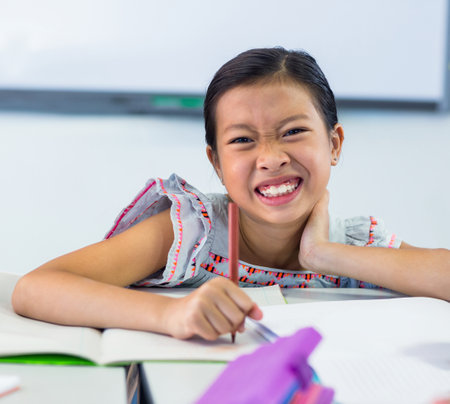 Portrait of smiling schoolgirls writing on books in classroomの写真素材