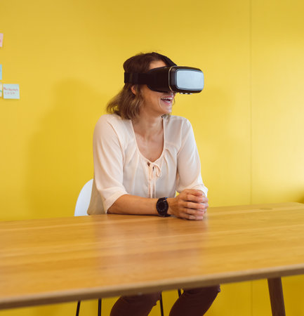 Woman sitting at wooden table in office, with VR headset, smartwatch and pastel sticky notes....
